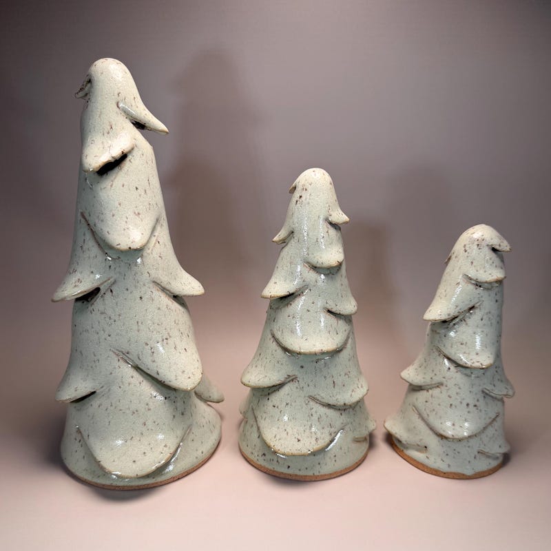 Three hand-built ceramic Christmas trees of graduating height in a speckled pale glaze.