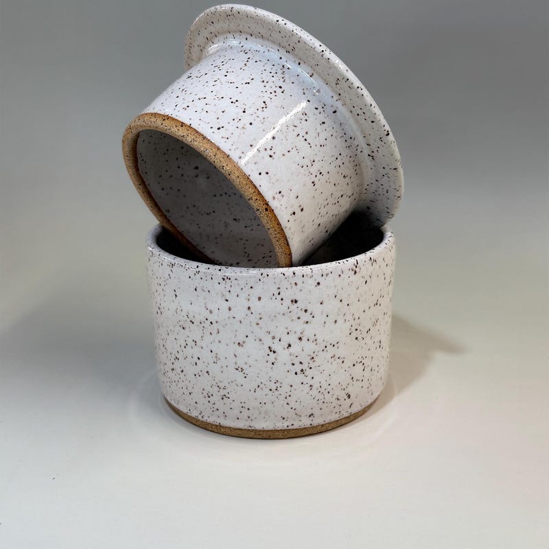 A two-part speckled white French butter dish, the lid resting at an angle on its base.