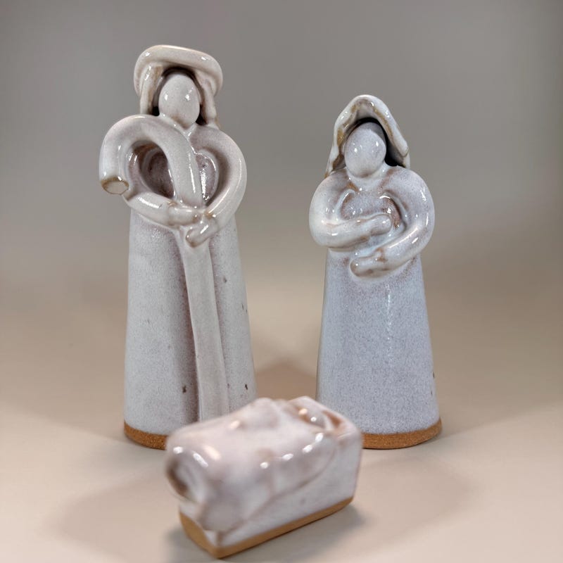 Three hand-sculpted nativity pieces in a soft white glaze: two standing figures and the manger.