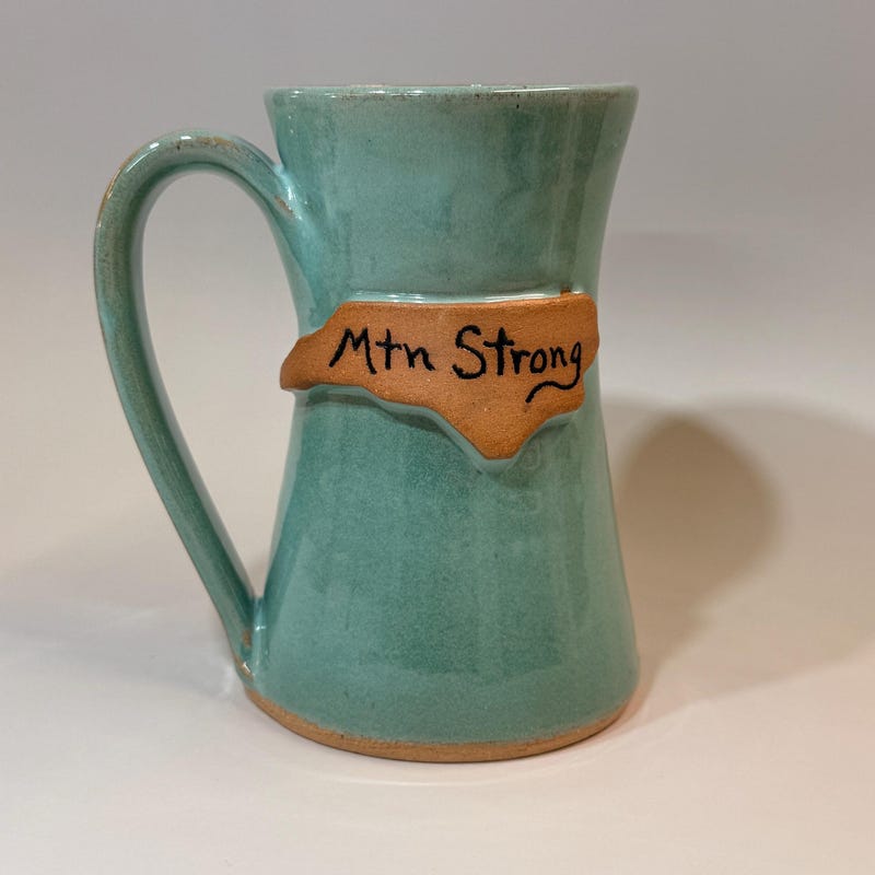 Sea green mug with the outline of North Carolina in bare clay, hand lettered Mtn Strong.
