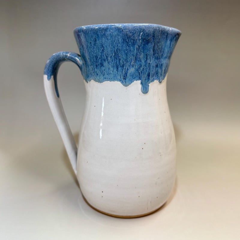 Tall white stoneware pitcher, a blue glaze breaking and running down from the rim.