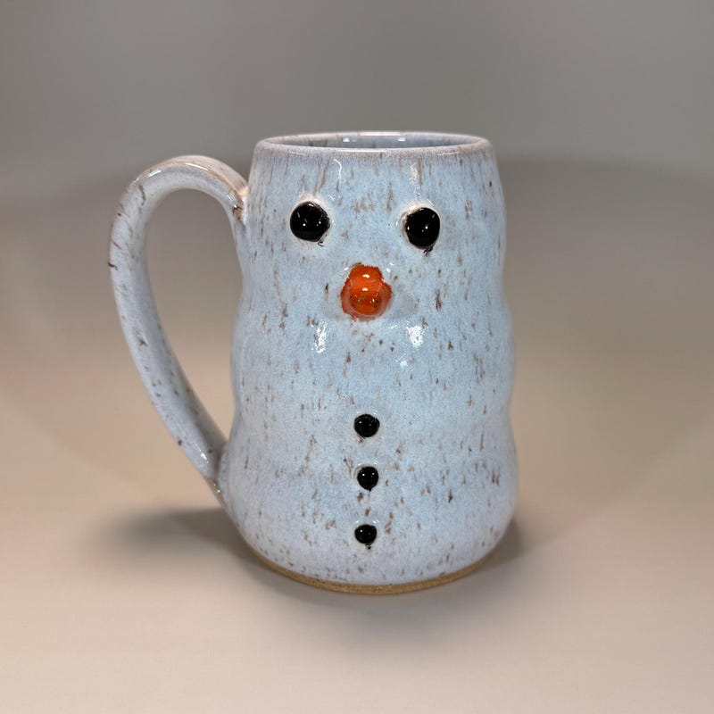 Pale blue speckled mug sculpted as a snowman, with a carrot nose and coal buttons.