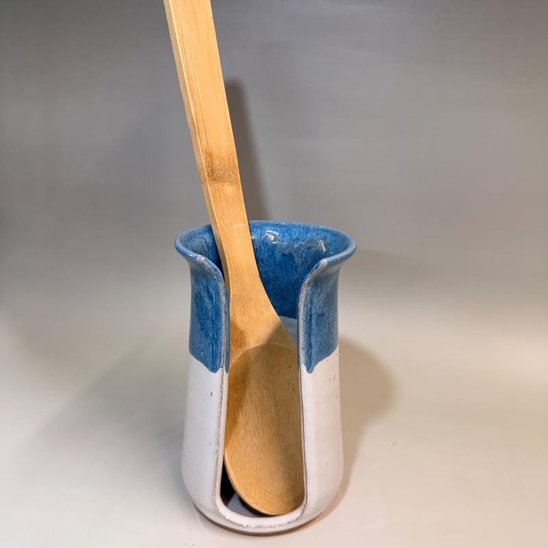 Blue and white ceramic holder with an open slot down one side, holding a wooden spoon.