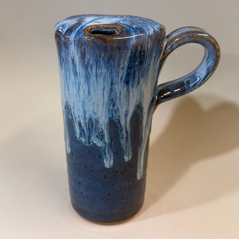 Tall blue travel mug with a built-in lid and drinking slot, white glaze running down over deep blue.